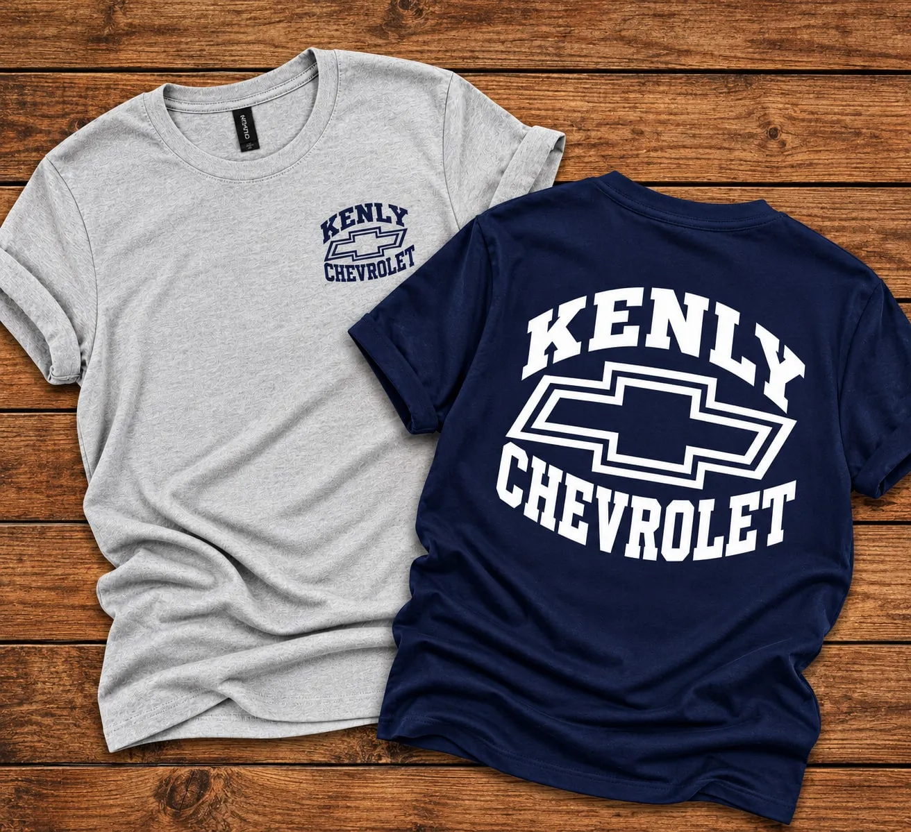 Two t-shirts with an arched Kenly Chevrolet bowtie design: navy print on the chest of a heather grey tee, and white print across the back of a navy tee.